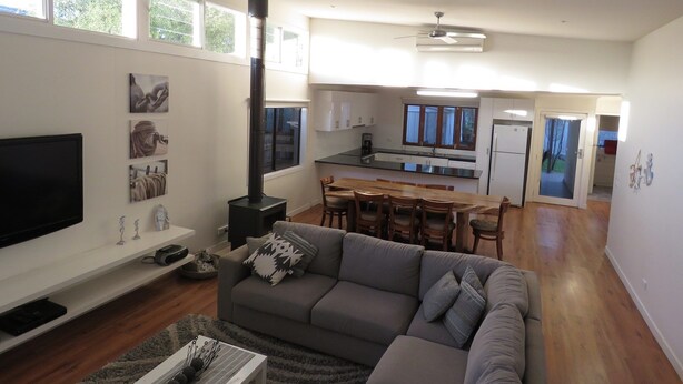 A modern living room with a sofa, TV, and fireplace. There is a kitchen with a dining area and a hallway leading to a door. - Genesta Street, sleeps 14 people, in the heart of Cowes (Cowes)