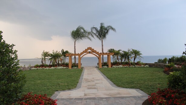 Un sendero que conduce a un arco de madera, flanqueado por palmeras y macizos de flores.