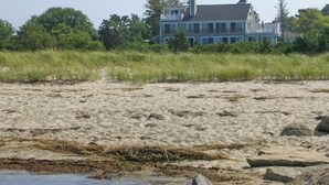 A beach with sand, rocks, and a house in the background. - Expansive Home With Gorgeous Bay Views! (1052) (Brewster)