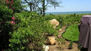 A garden with a lawn, rocks, and flowering plants. - Expansive Home With Gorgeous Bay Views! (1052) (Brewster)