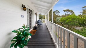 A covered porch with a railing, a door with a window, and a bench.