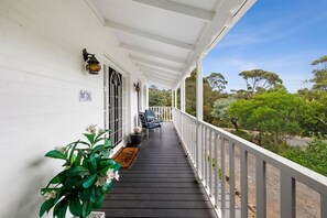 A covered porch with a railing, a door with a window, and a bench. - Noble Villa (Anglesea)