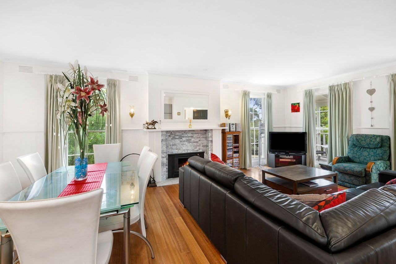 A modern living room with a glass dining table, leather sofa, and a fireplace.