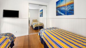 A hotel room with two beds, a TV, and a painting of a sunset over the ocean.