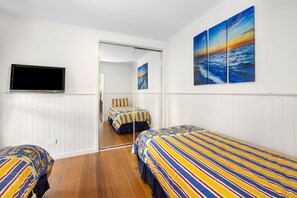 A hotel room with two beds, a TV, and a painting of a sunset over the ocean. - Noble Villa (Anglesea)