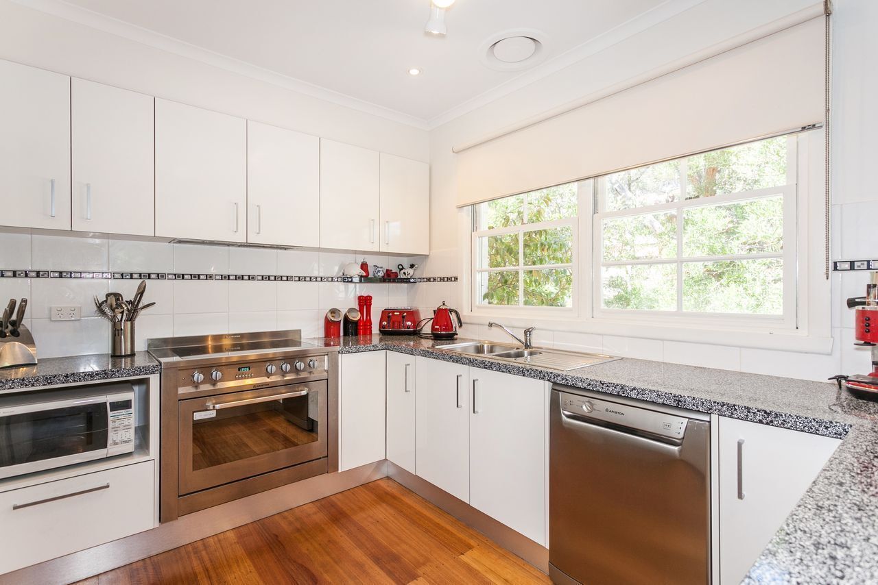 A modern kitchen with stainless steel appliances, white cabinetry, and a large window providing natural light.