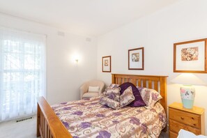 A bedroom with a bed, a chair, a bedside table with a lamp, and framed pictures on the wall.