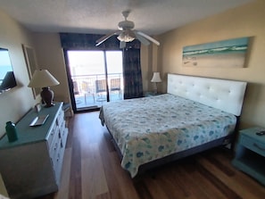 A bedroom with a bed, a desk, a dresser, a ceiling fan, and a balcony with a view.