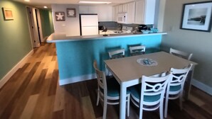 A modern kitchen with white cabinets, a blue island, and a dining area with white chairs. - Panoramic Views from spacious 3 BR 2 BA condo (Myrtle Beach)