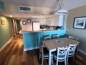 A modern kitchen with white cabinets, a blue island, and a dining area with white chairs.