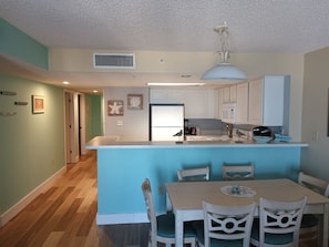 A modern kitchen with white cabinets, a blue island, and a dining area with white chairs and a table.