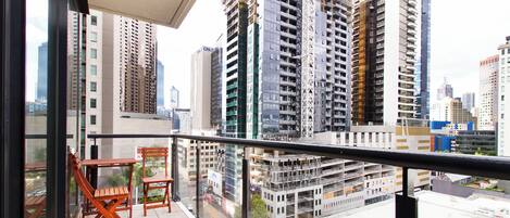 Enjoy the city view from this high-rise balcony with a table and chairs.