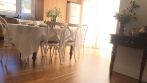 A dining area with a wooden table and chairs, a vase with flowers, and a view of the outside through a window.