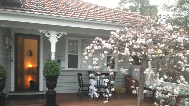 A house with a porch, a dining table set for two, and potted plants.