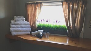 Una ventana con cortinas, una pila de toallas y una planta pequeña con flores moradas.