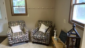 Una habitación con dos sillones estampados, una mesita de madera con una pizarra y una ventana con vistas a árboles.