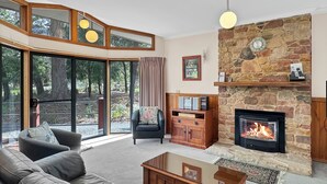 A living room with a stone fireplace, a sofa, a coffee table, and a television. - "School House Villa" hosted by Halls Gap Accommodation (Halls Gap)