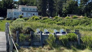 A wooden deck leading to a house surrounded by lush greenery and a clear blue sky. -  Luxury Waterfront Home with Pool and Dock  NEW 5% Discount Until Feb. 28th (eastham)
