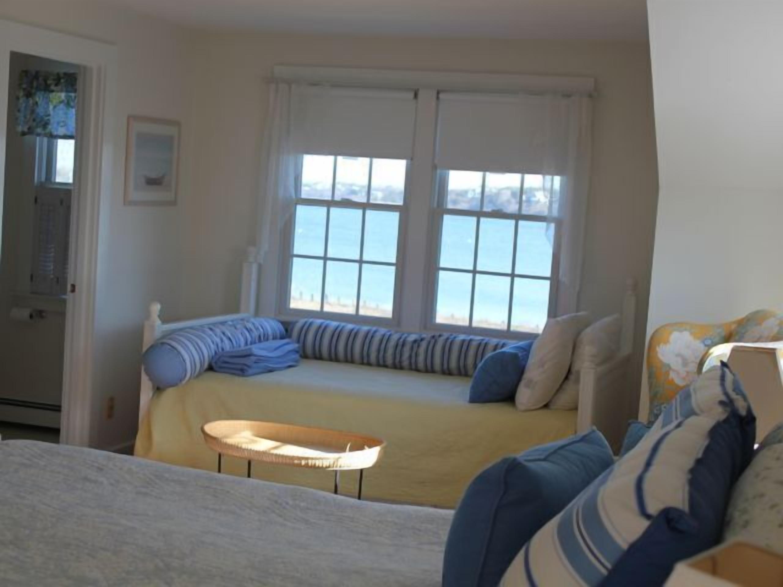 A bedroom with a bed, a small table, and a window with a view of the sea.