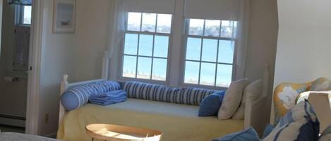 A bedroom with a bed, a small table, and a window with a view of the sea.