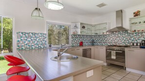 Een moderne keuken met een centraal eiland, roestvrijstalen apparatuur en een betegelde achterwand.