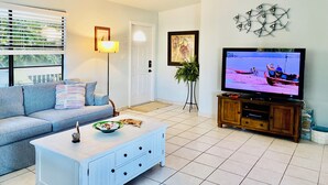 Un salon comprenant un canapé, une table basse, un téléviseur, un ventilateur de plafond et une porte.