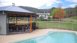 A covered outdoor seating area with a pool, a fenced patio, and a view of a hilly landscape.