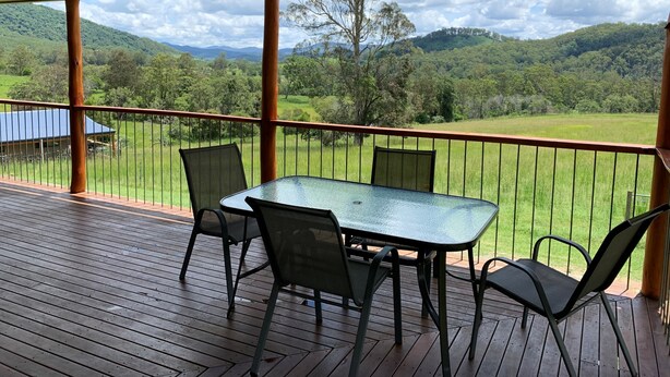 A covered outdoor area with a table and chairs, overlooking a green landscape with hills.