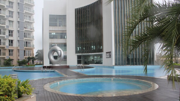 A modern hotel with a large outdoor swimming pool, a circular water feature, and a palm tree.