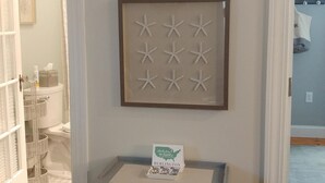 Une salle de bain comprenant des toilettes, un lavabo et un espace douche. On y trouve une petite table sur laquelle est posé un panneau.