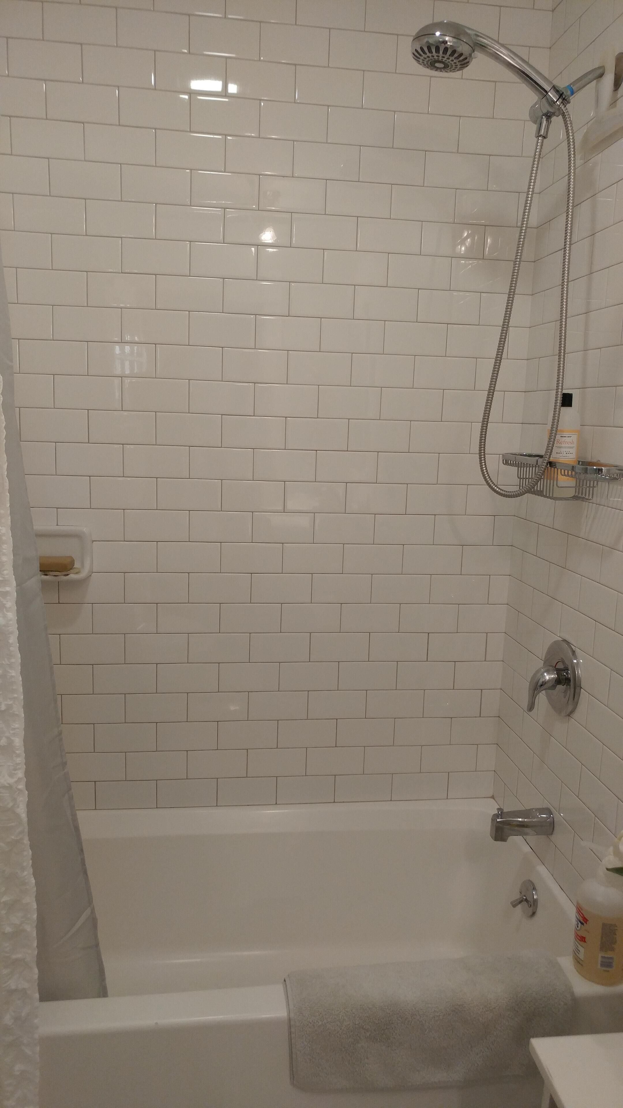 Une salle de bain avec des murs carrelés de carreaux blancs, une baignoire, une douche et une serviette sur le sol.