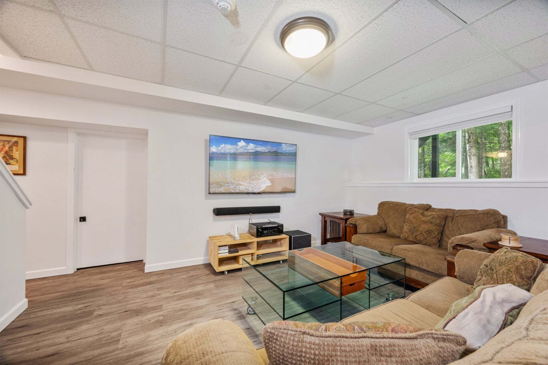 Una sala de estar con una mesa de centro de vidrio, un sofá, un televisor y un cuadro con una escena de playa.