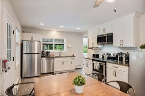 A modern kitchen with white cabinetry, stainless steel appliances, and a wooden dining table.