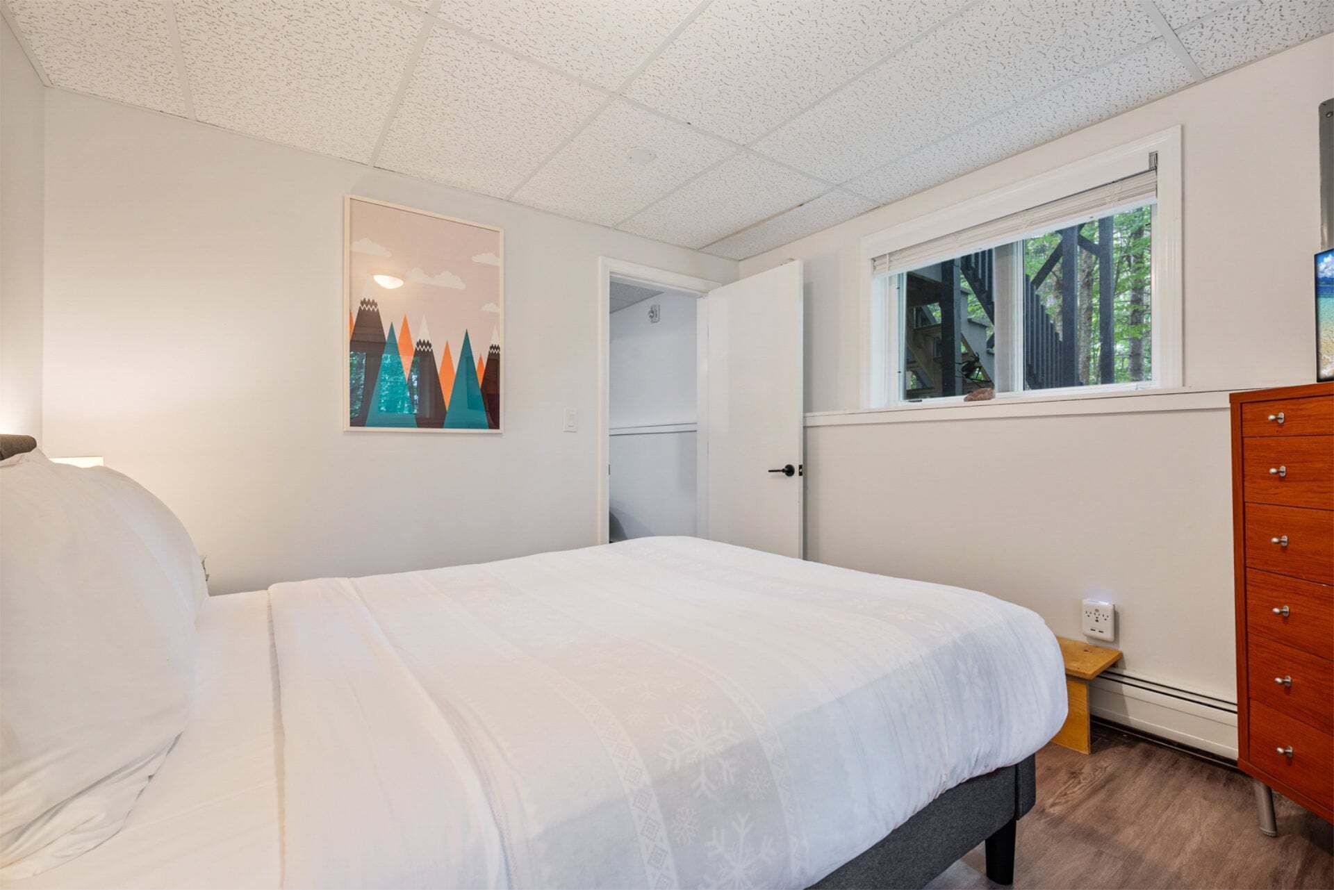 A bedroom with a bed, a dresser, a window, and a door leading to another room.