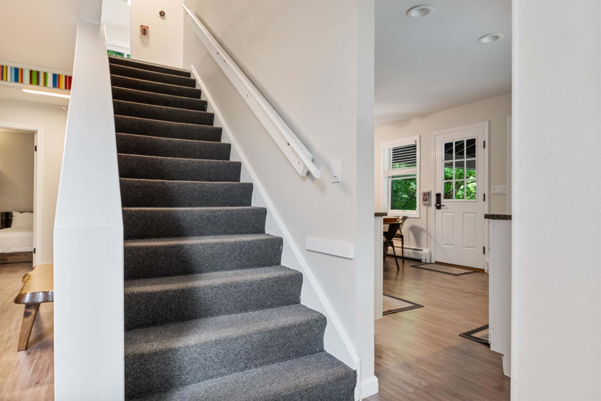 A staircase with carpeted steps leading to a landing, a white door, and a window with blinds.