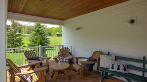 A wooden deck with outdoor furniture, including chairs and a bench, overlooking a grassy area with trees and a distant building. - Private Family Estate for any Season - Hermitage Club/Inn (West Dover)