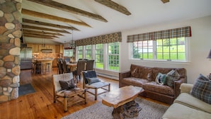 A rustic interior with exposed wooden beams, stone walls, a stone pillar, a wooden dining table with chairs, a leather sofa, and large windows with plaid curtains. - Private Family Estate for any Season - Hermitage Club/Inn (West Dover)