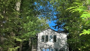 Une cabane avec un mur en pierre, une terrasse en bois et des fauteuils Adirondack.