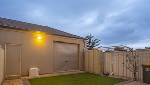 Un jardin arrière d’une maison, avec une terrasse dallée, une pelouse, un garage et une clôture.