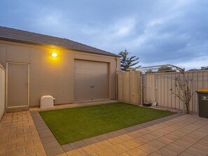 Ein Wohngrundstück mit gepflasterter Terrasse, Rasenfläche, Garage und Zaun.