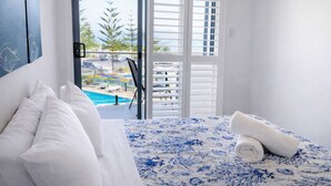 Un dormitorio con cama, almohadas blancas, colcha de flores azules y vistas a una piscina y árboles a través de una puerta corredera.