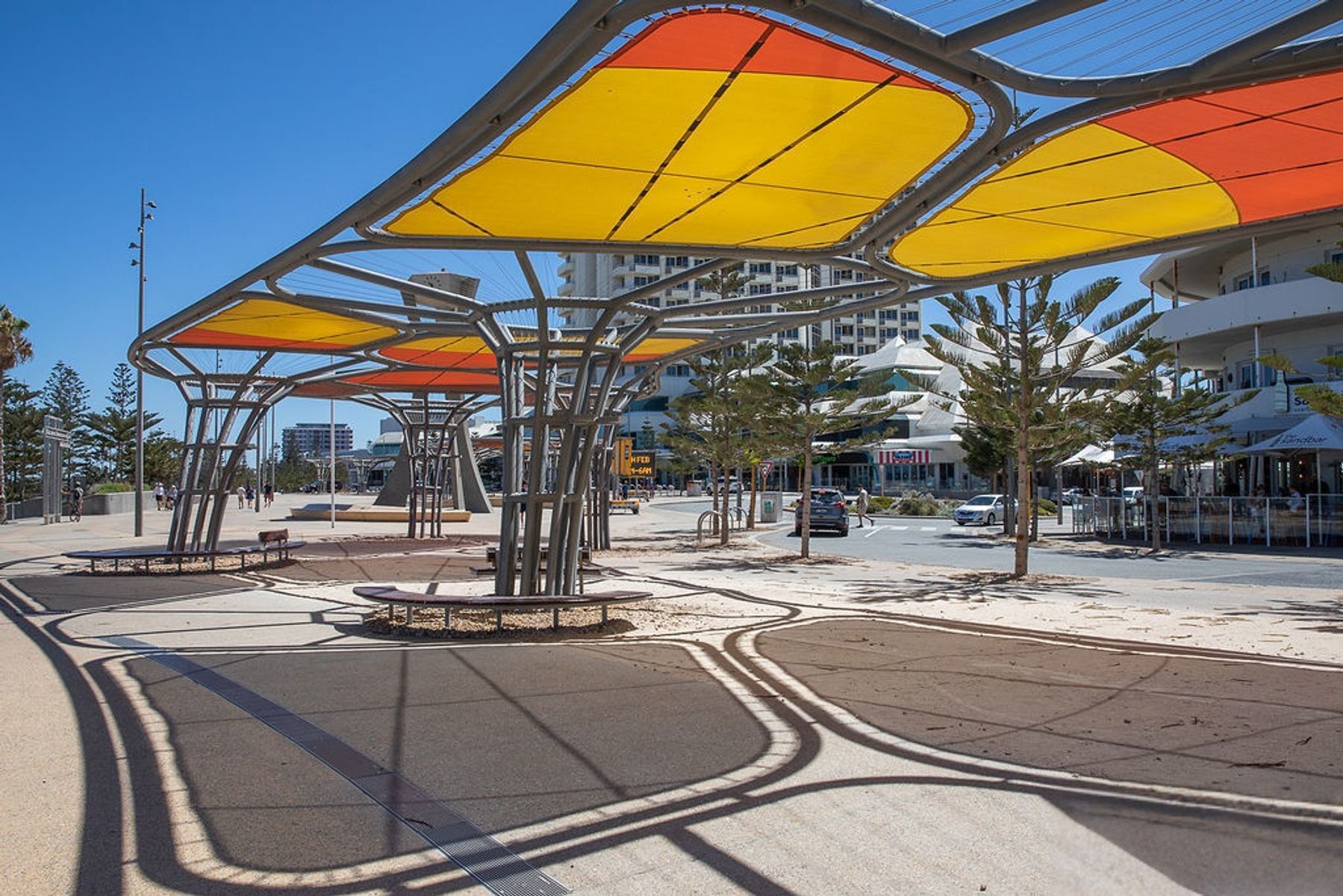 A public square with modern, abstract metal structures providing shade.
