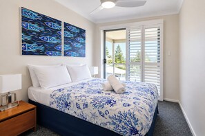 Habitación de hotel con cama, mesita de noche, lámpara y ventana con persianas.
