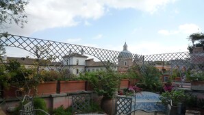 A patio with a round table and chairs, surrounded by potted plants and a decorative fence. - luxury penthouse in the heart of Rome with two terrific terraces on the domes (rome)