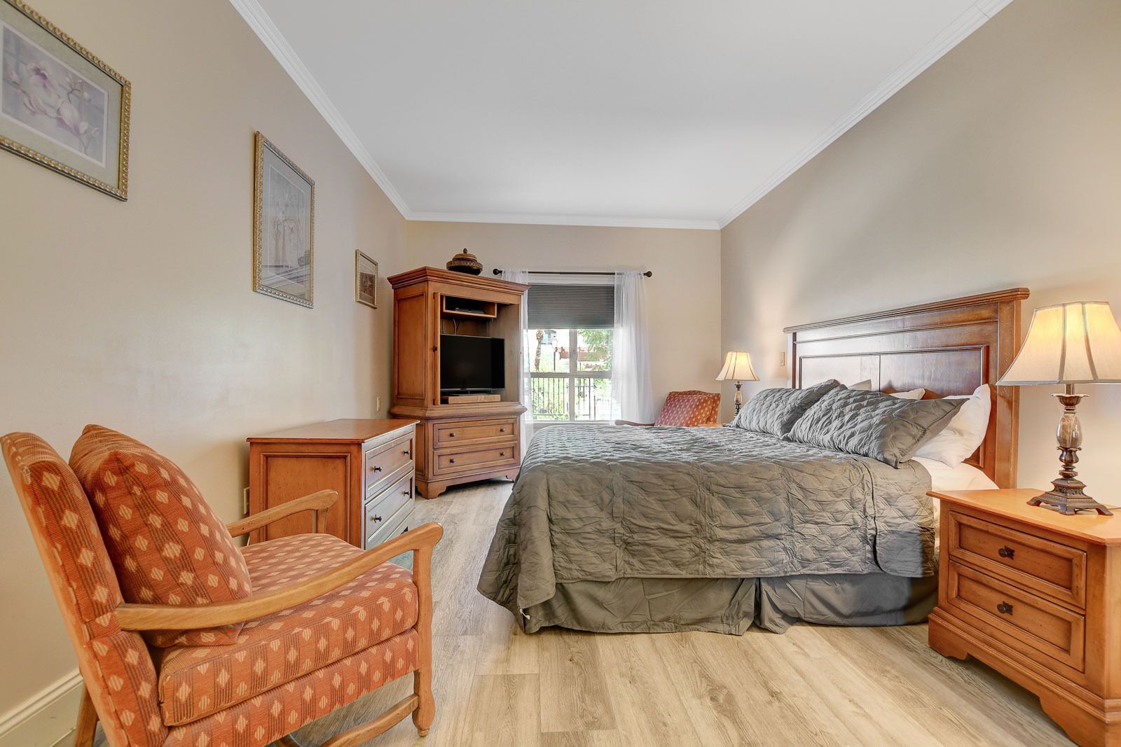 A bedroom with a bed, wooden nightstands, a chair, a dresser, and a television.