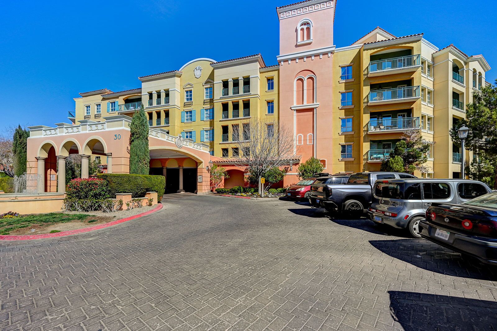 A multi-story hotel with a central courtyard, a clock tower, and a parking area with several vehicles.