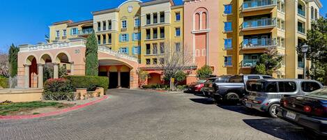 A multi-story hotel with a central courtyard, a clock tower, and a parking area with several vehicles.