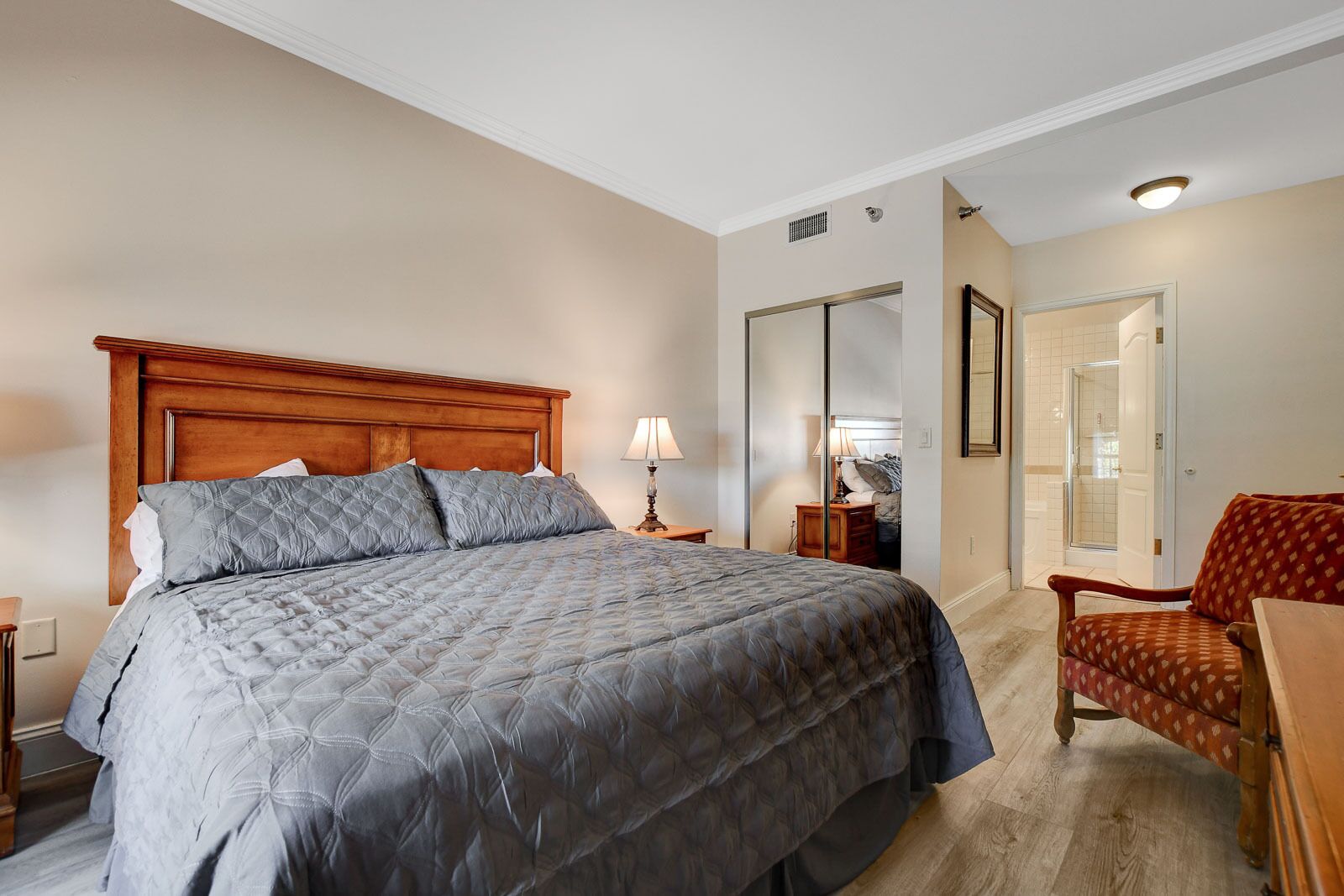 Un dormitorio con una cama grande, una mesita de noche, una silla, un espejo y un vestidor.