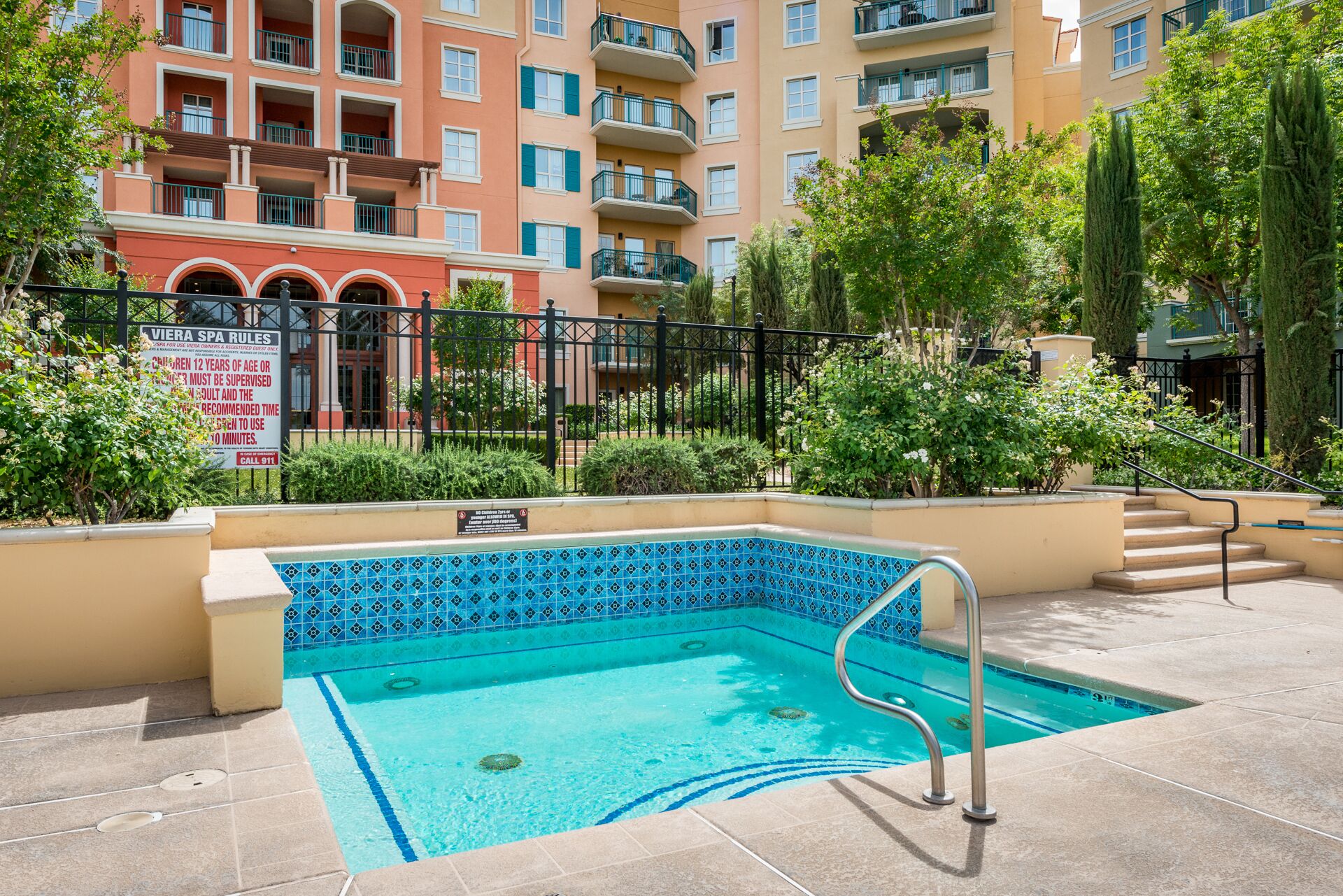 Una piscina con diseño de azulejos azules, rodeada por una valla y vegetación.