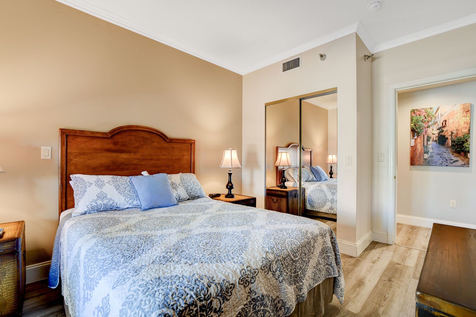 A hotel room with a large bed, a nightstand, a mirror, and a painting on the wall.